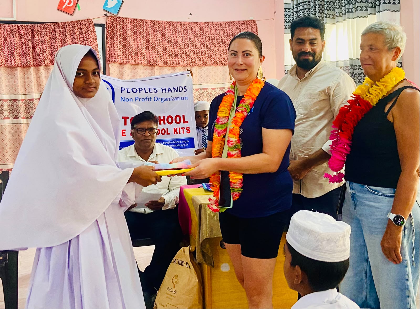 Amandine from France presenting stationery to a student in Kuchchaveli, Trincomalee, alongside People's Hands Organization staff